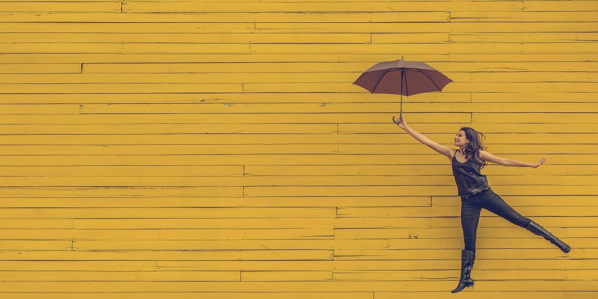 woman in black with umbrella flying across a yellow wall symbolising benefits of executive coaching