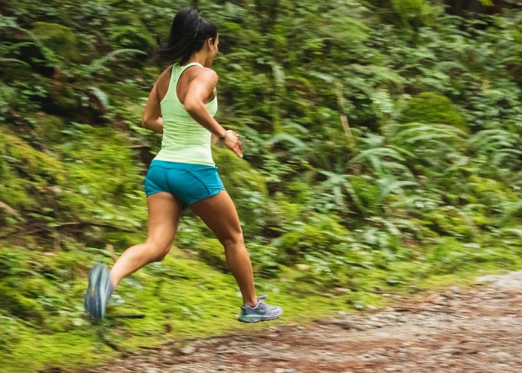 black woman running through green ferns on brown path