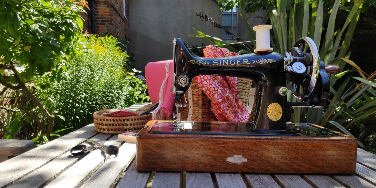An antique sewing machine, scissors and fabric on a table in a garden symbolising the author's resilience
