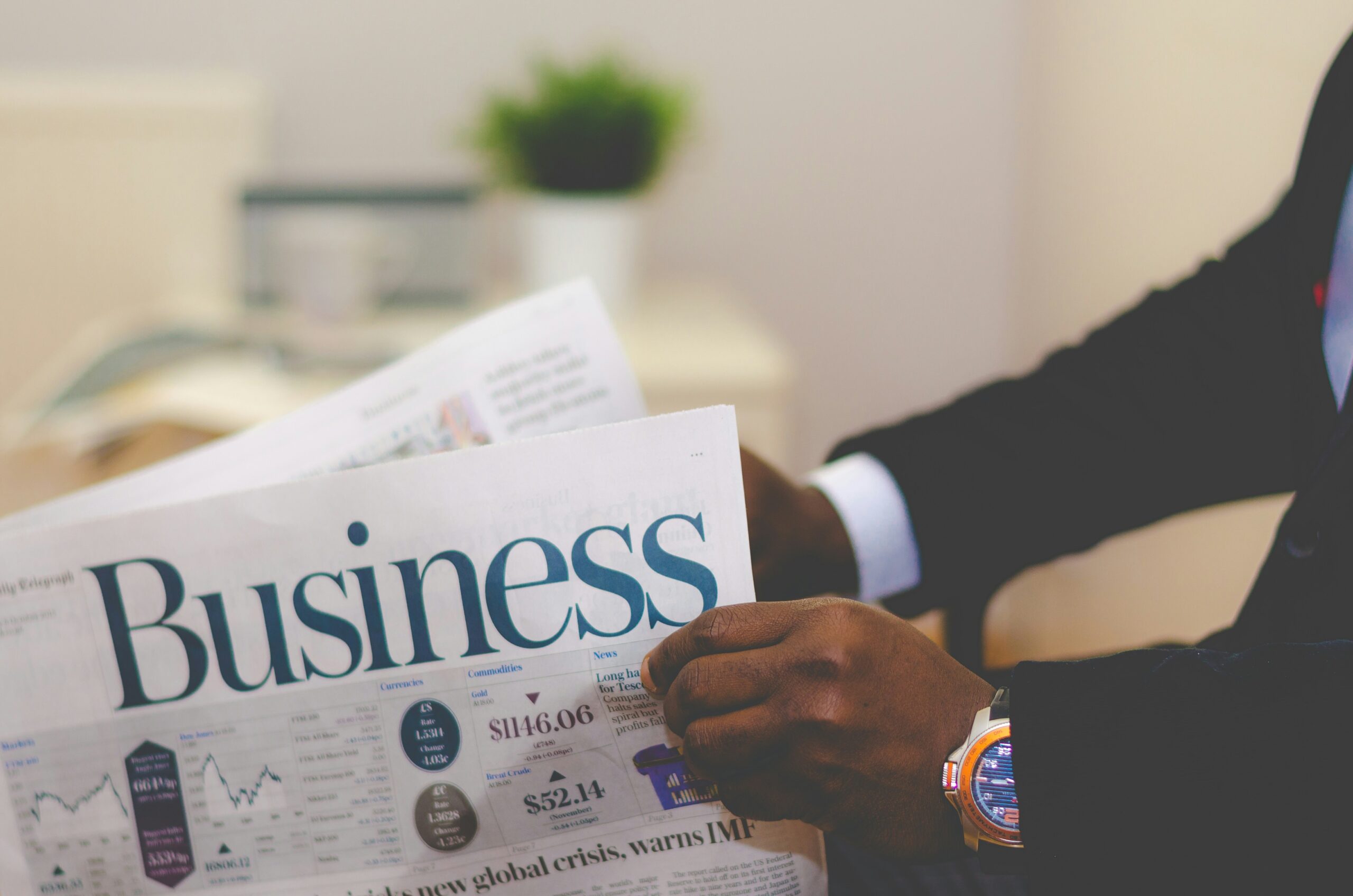 adeolu-eletu-E7RLgUjjazc-unsplash picture of a black man's hands holding a business newspaper. The man is wearing a dark suit and a white shirt. The newspaper signifies development of people management skills